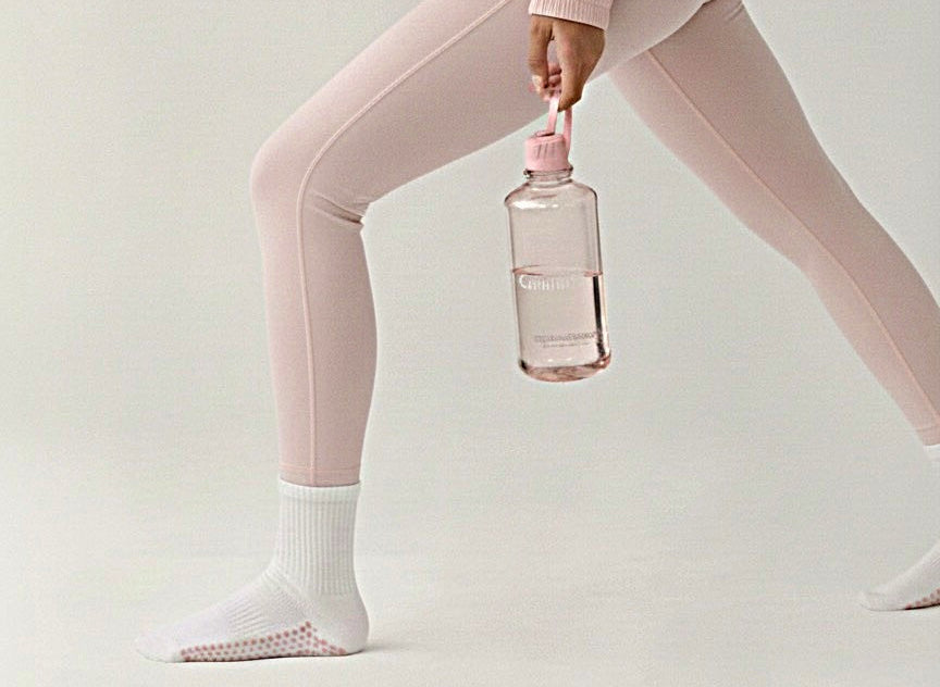 Person wearing a pink grip socks holding a pink water bottle on a light gray background